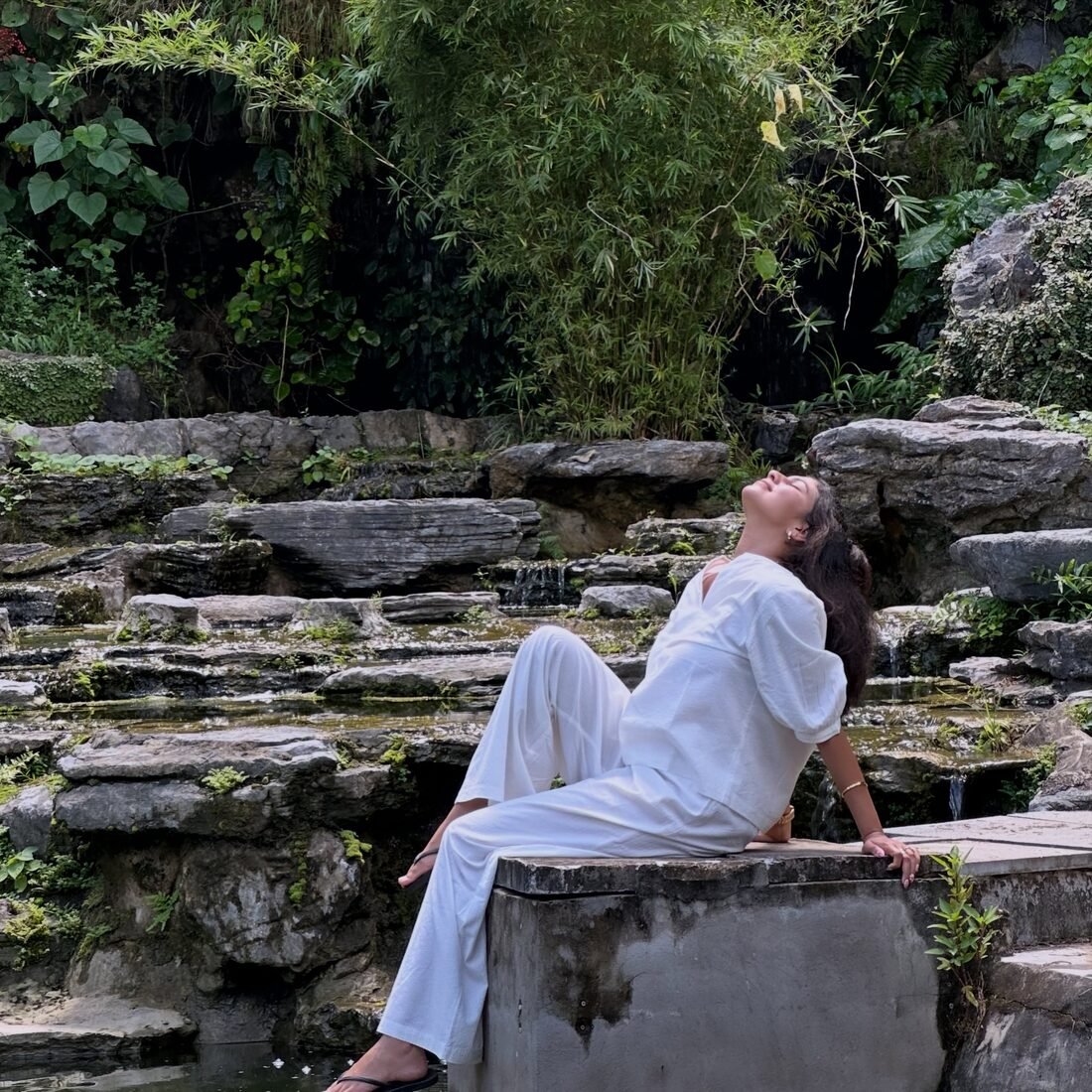 Shreya Jadhav seated on a rock ledge beside a waterfall garden